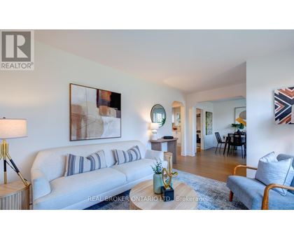 A living room with a white couch and a painting on the wall.