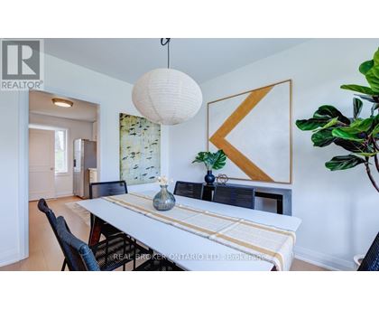 A dining room with a white table and chairs, a hanging light fixture, and a large plant.