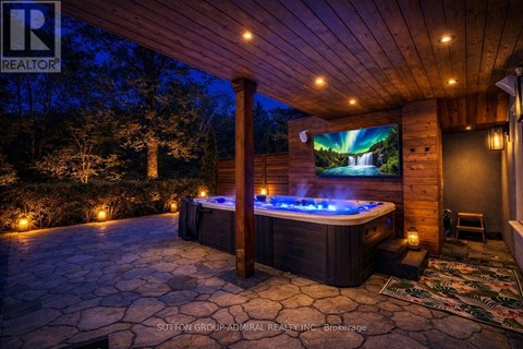 A hot tub sits in the middle of a stone patio under a lit-up wooden pergola.