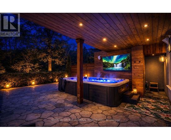 A hot tub sits in the middle of a stone patio under a lit-up wooden pergola.