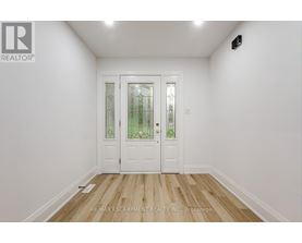A white door with a glass panel and a black handle is in a room with white walls and wooden flooring.