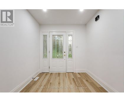 A white door with a glass panel and a black handle is in a room with white walls and wooden flooring.