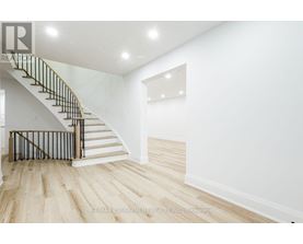 A white interior space with a wooden staircase and light wood flooring.