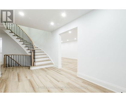 A white interior space with a wooden staircase and light wood flooring.