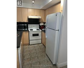 A white refrigerator stands in a kitchen with a black microwave and white stove.