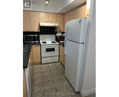 A white refrigerator stands in a kitchen with a black microwave and white stove.