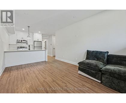 A living room with a grey couch and a kitchen area in the background.