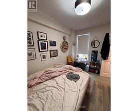 A bedroom with a bed covered in a pink comforter and a wooden wall hanging.