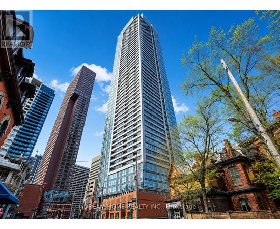 A tall building stands in front of a tree and other buildings.