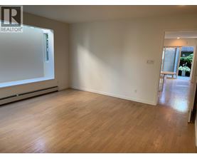 A room with wooden flooring and white walls, with a door leading to another room.