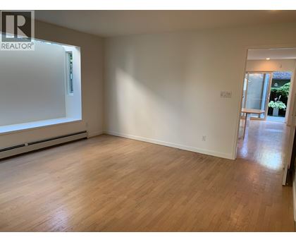 A room with wooden flooring and white walls, with a door leading to another room.