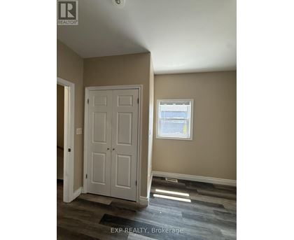 A room with a white door and a window with a view of a fence and trees.