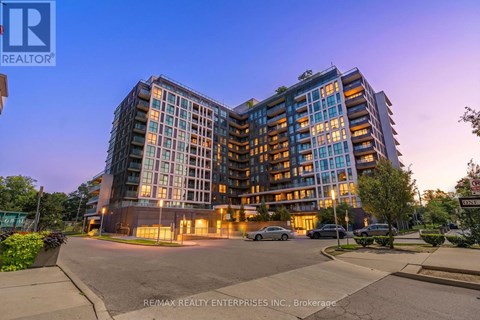 A modern multi-story building with a parking lot in front.