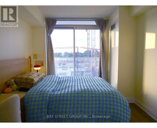 A bedroom with a bed, nightstand, and window overlooking a construction site.