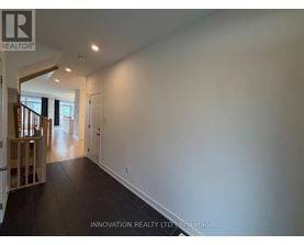 A spacious room with white walls and dark flooring, part of a house showing a staircase.
