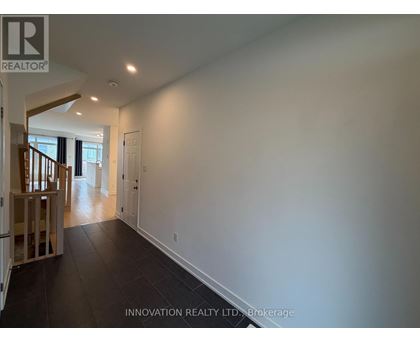 A spacious room with white walls and dark flooring, part of a house showing a staircase.