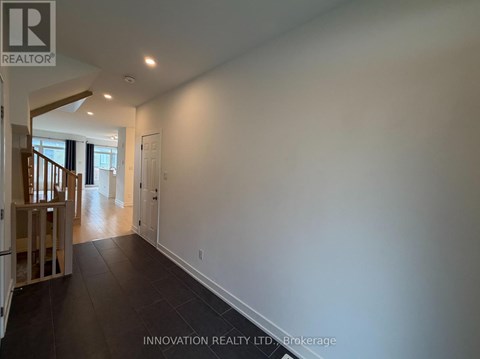 A spacious room with white walls and dark flooring, part of a house showing a staircase.