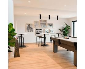 A pool table is in the middle of a room with a light wood floor and a white wall with pictures hanging on it.