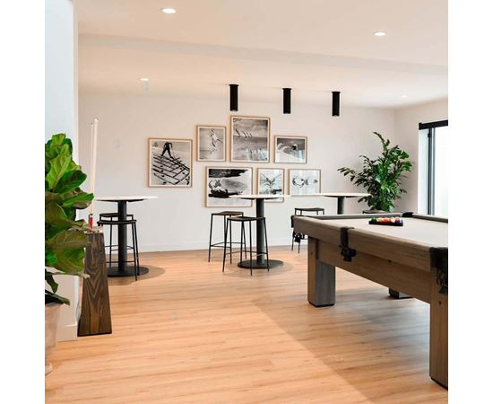 A pool table is in the middle of a room with a light wood floor and a white wall with pictures hanging on it.