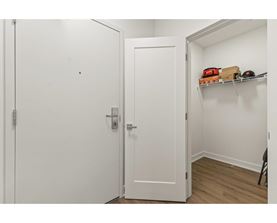 A white door with a silver handle is open to a hallway with a shelf and a chair.