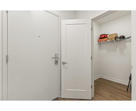 A white door with a silver handle is open to a hallway with a shelf and a chair.