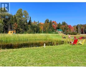 A serene lakeside setting with a yellow house and a green house in the background, surrounded by trees with autumn foliage.