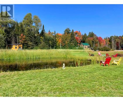 A serene lakeside setting with a yellow house and a green house in the background, surrounded by trees with autumn foliage.