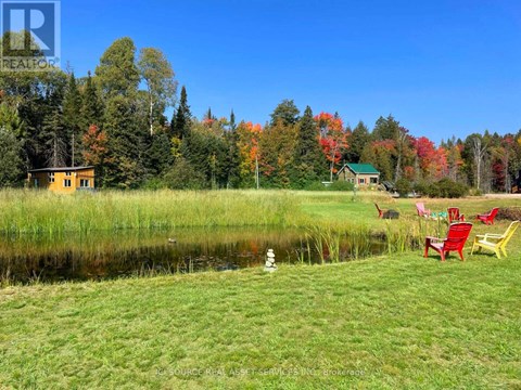 A serene lakeside setting with a yellow house and a green house in the background, surrounded by trees with autumn foliage.