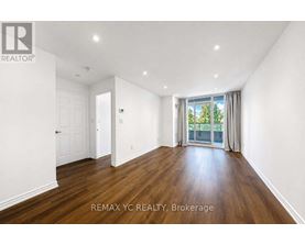 A spacious room with wooden floors and white walls, with a sliding glass door leading to a balcony.