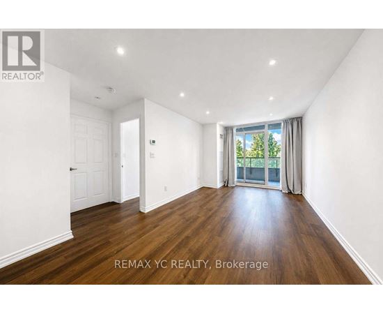A spacious room with wooden floors and white walls, with a sliding glass door leading to a balcony.