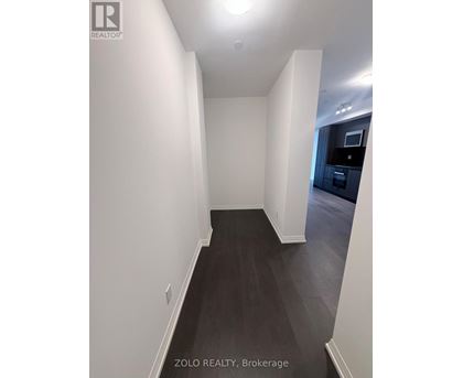 A hallway with white walls and dark wood flooring.