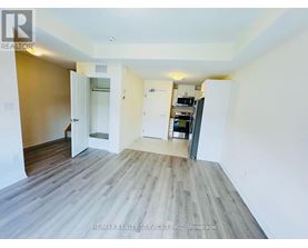 A room with a wooden floor and white walls, with a door open to another room.