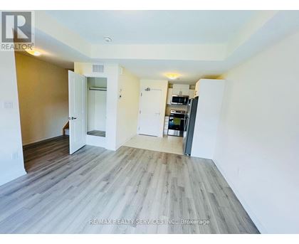 A room with a wooden floor and white walls, with a door open to another room.