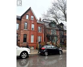 A black car is parked on a wet street in front of a red brick house.