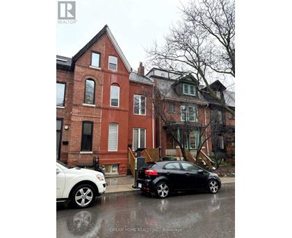 A black car is parked on a wet street in front of a red brick house.