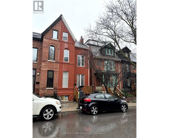 A black car is parked on a wet street in front of a red brick house.
