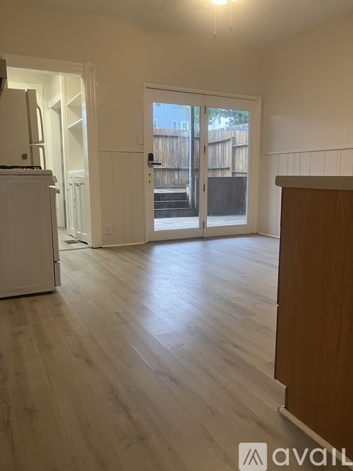 A room with wooden flooring and white walls, with a door in the background.