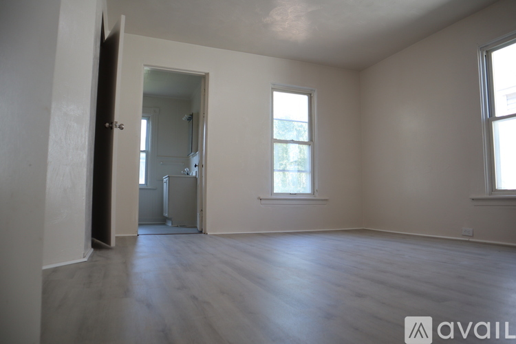 A spacious room with wooden floors and two windows.