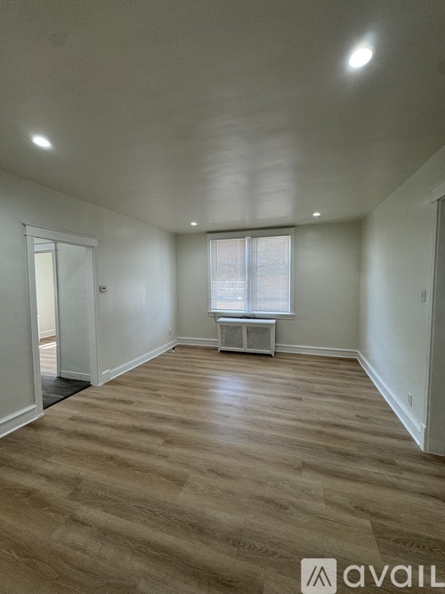 A spacious room with wooden flooring and a window with blinds.