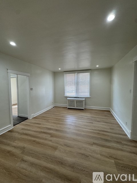 A spacious room with wooden flooring and a window with blinds.