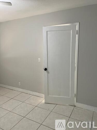 A white door with a black handle is in a room with white walls and tile flooring.