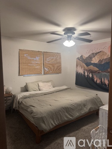 A bedroom with a bed, a ceiling fan, and a mountain mural on the wall.