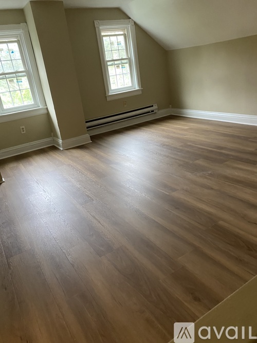 A room with wooden flooring and two windows.