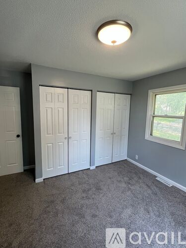 A room with grey carpet and a window with a white frame.
