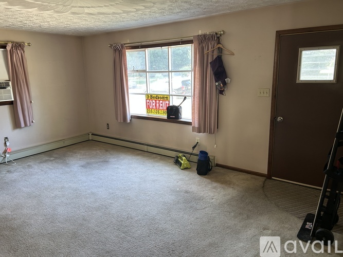 A room with a carpeted floor, a window with a sign that says "9 Bedrooms FOR RENT" and a door.