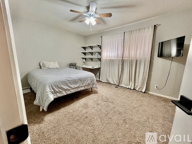 A bedroom with a bed, a ceiling fan, and a television.