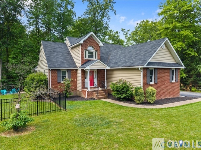 A house with a red door and a brick chimney is surrounded by a green lawn and trees.