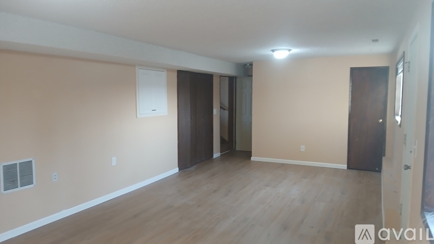 A spacious room with wooden flooring and a large window on the left side.