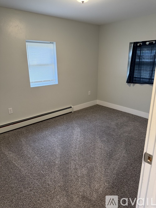 A room with a carpeted floor, a window with blinds, and a door.