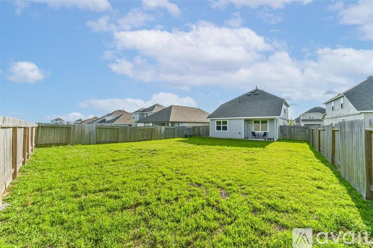 A grassy backyard with a house and fence in the background.